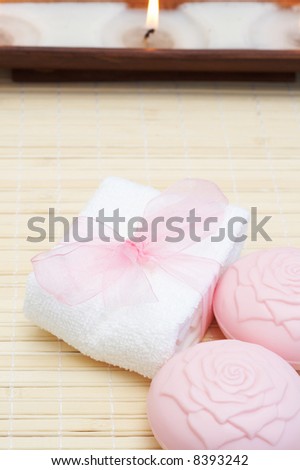 Relaxing spa scene with white face towel, pink beauty soap and candles in the background