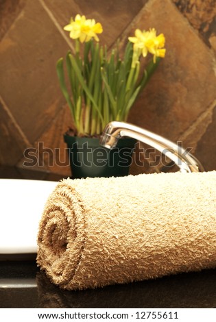 Beige rolled up towel next to a white ceramic basin with daffodil flowers in the bathroom