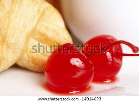 Macro shot of glazed maraschino cherries on white plate with fresh croissant at the back