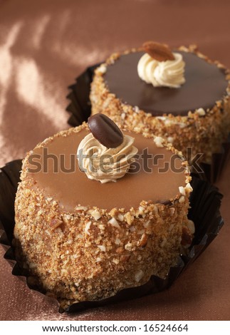 Miniature chocolate meringue cakes with cream and almonds on golden silk background