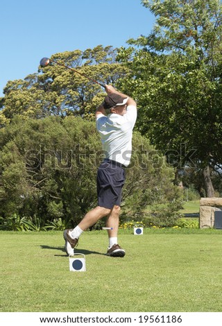 Senior golfer hitting the ball off the tee box. Peg flying past the left leg. Nice summer day