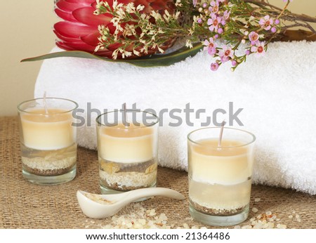 Relaxing spa scene with a white rolled up towel, red protea, beautiful handmade candles and bath salts
