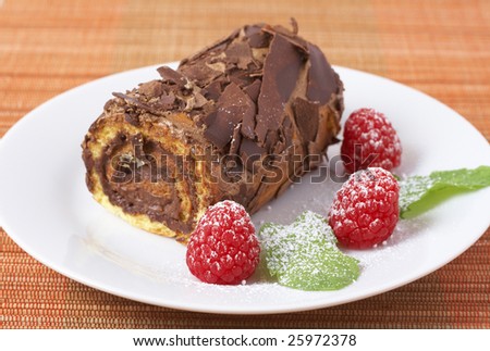 Miniature chocolate swiss roll cake served on a plate with mint leaves and raspberries on orange background