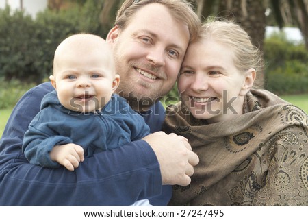 Beautiful happy family of three posing in their garden laughing. Focus is on the father