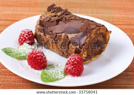 Miniature chocolate swiss roll cake served on a plate with mint leaves and raspberries on orange background