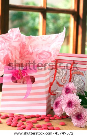 Two pink gift bags with pink candy scattered around it
