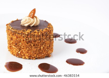 Miniature chocolate meringue cake with cream and almonds, served on a plate with sauce drops