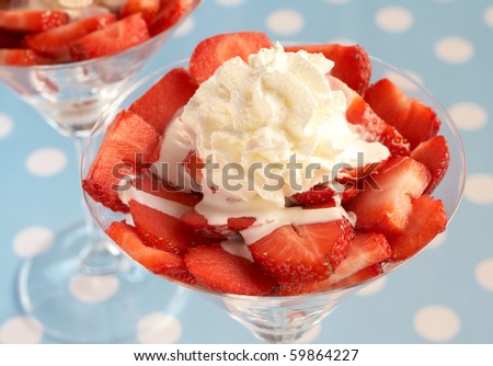 Sliced fresh strawberries with cream in martini glasses on blue polka dot background