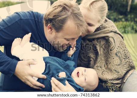 Beautiful happy family of three sitting on the grass laughing. Focus is on the father
