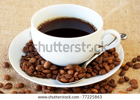 Cup of fresh brewed coffee with roasted coffee beans on straw placemat