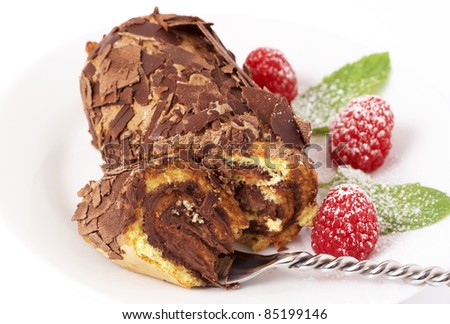 Miniature chocolate swiss roll cake served on a plate with mint leaves and raspberries on white background