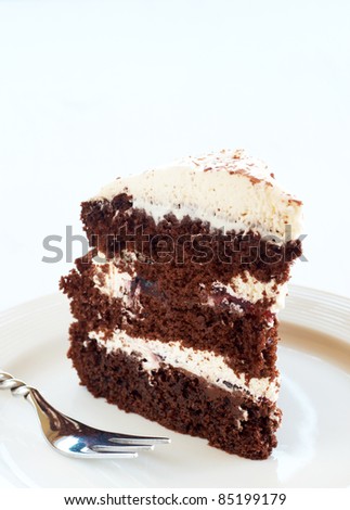 Slice of Black Forest cake with fresh cream and cherries, served on a white plate with silver fork
