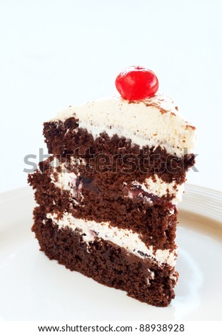 Slice of Black Forest cake with fresh cream and cherries, served on a white plate