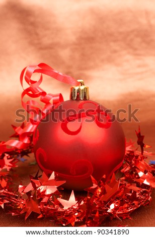 Single red Christmas bauble with star tinsel on golden silk background