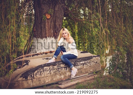 Young pretty woman sitting on the old boat near the lake in spring