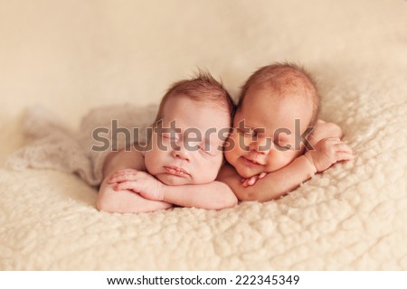 Newborn twins sleeping on the beige blanket together