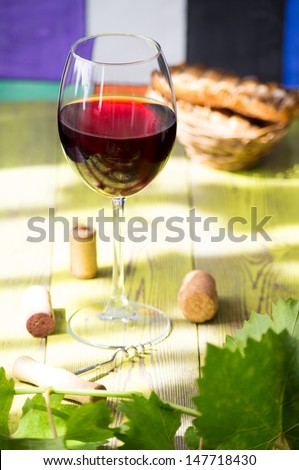 Glass of red wine on a wooden table with leaves of grapes, corkscrew and wine corks and toast.