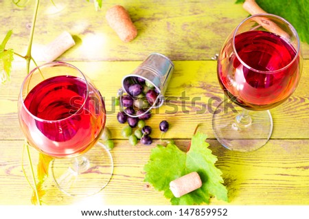 Two glasses of red wine on the background of an old brick wall and grape vines. Behind to a bucket of grape berries, corkscrew and wine corks