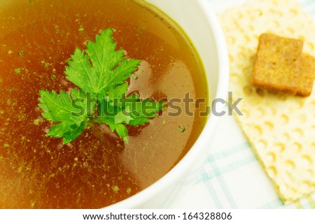 Bouillon, broth, clear soup in a white cup with a loaf, parsley on the tablecloth. Close-up.