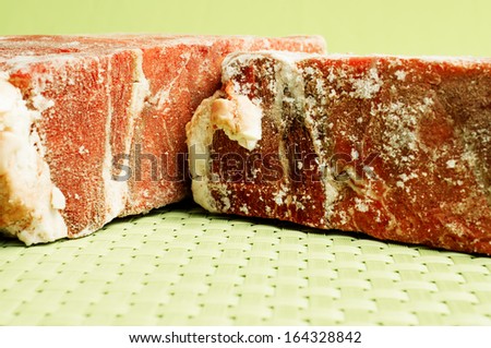 Frozen meat. Two pieces of frozen beef meat on a green background.