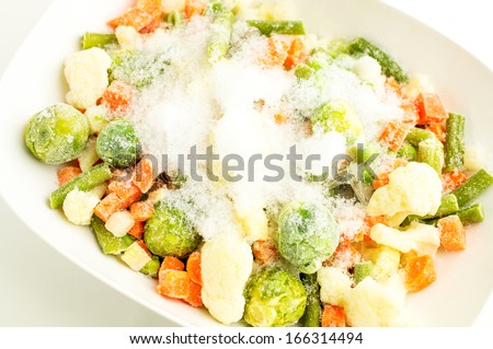 Mixture of frozen vegetables, carrots, peas, broccoli, green beans, Brussels sprouts, cauliflower in white bowl with ice and snow. For background.