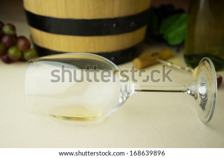 White wine in a glass lying. Background wine barrel, bottle of white wine, corkscrew, cork and grapes.