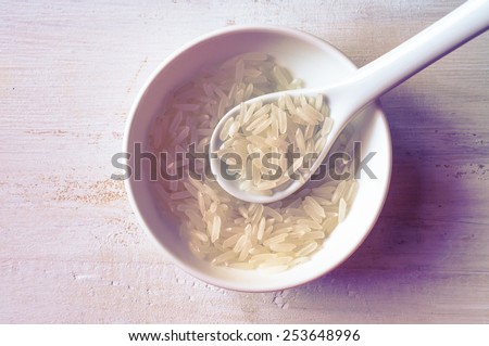 Jasmine rice grains in a white spoon on white table. Top view