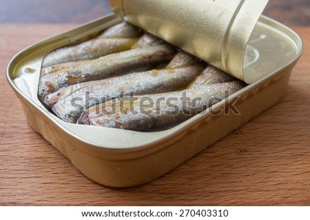 Open can of sardines on a wooden board