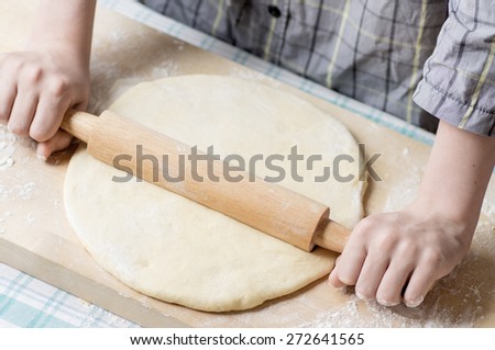 Hands teenage boy with a rolling pin roll the dough for pizza