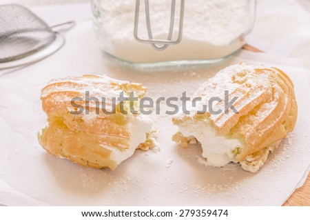 Cake eclair custard is broken in half on a table with a jar of powdered sugar