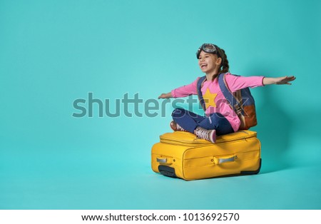 Dreams of travel! Child flying on a suitcase on background of bright blue wall.