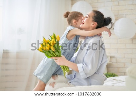 Happy mother\'s day! Child daughter is congratulating mom and giving her flowers tulips. Mum and girl smiling and hugging. Family holiday and togetherness.