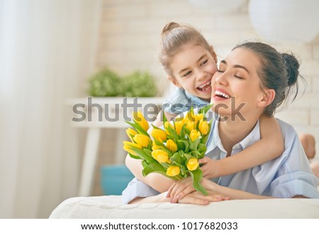Happy mother\'s day! Child daughter is congratulating mom and giving her flowers tulips. Mum and girl smiling and hugging. Family holiday and togetherness.