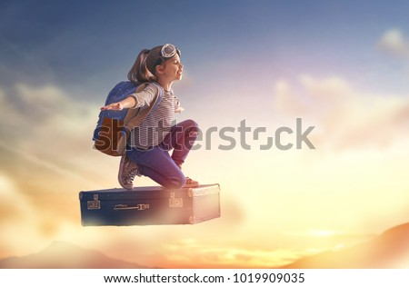 Dreams of travel! Child flying on a suitcase against the backdrop of sunset.