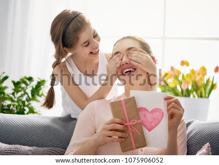 Happy women\'s day! Child daughter is congratulating mom and giving her postcard and gift. Mum and girl smiling and hugging. Family holiday and togetherness.