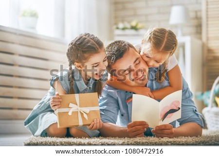 Happy father\'s day! Children daughters congratulating dad and giving him postcard and gift box. Daddy and girls smiling and hugging. Family holiday and togetherness.