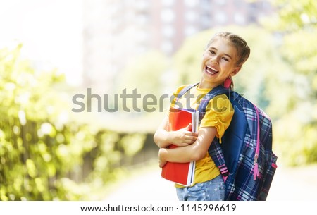 Pupil of primary school with book in hand. Girl with backpack near building outdoors. Beginning of lessons. First day of fall.