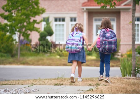 Pupils of primary school. Girls with backpacks near building outdoors. Beginning of lessons. First day of fall.