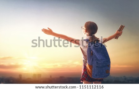 Pupil of primary school with book in hand. Girl with backpack on sunset background. Beginning of lessons. First day of fall.