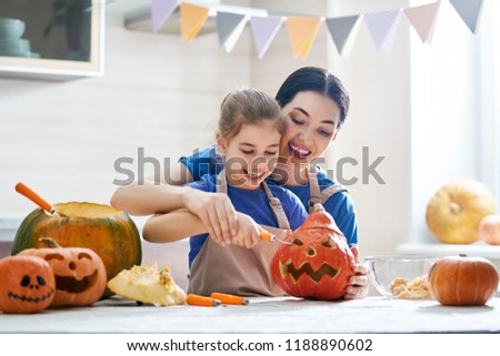Happy Halloween! Mother and her daughter carving pumpkin. Family preparing for holiday.