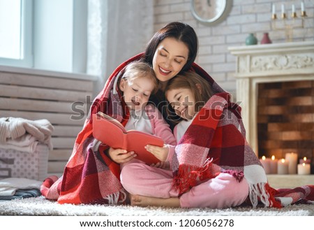 Winter portrait of happy loving family. Pretty young mother reading a book to her daughters at home.