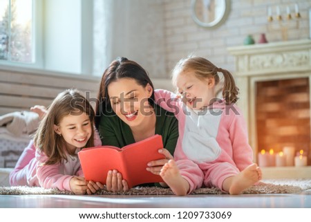 Winter portrait of happy loving family. Pretty young mother reading a book to her daughters at home.