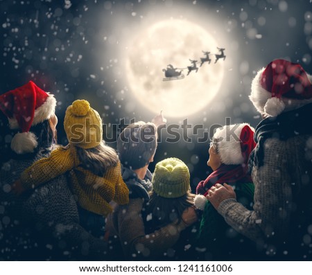 Merry Christmas and happy holidays! Cute little children with mom, dad, grandma and grandpa. Santa Claus flying in his sleigh against moon sky. Family enjoying the holiday on dark background.