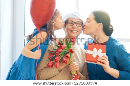 Happy women\'s day! Child daughter is congratulating mom and granny giving them flowers tulips. Grandma, mum and girl smiling and hugging. Family holiday and togetherness.
