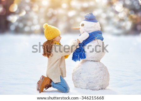 Happy child girl playing with a snowman on a winter walk in nature