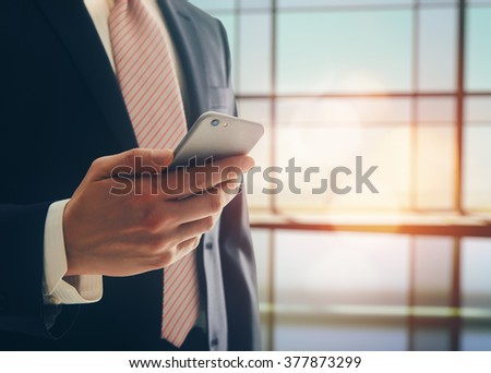Portrait of a confident man. Entrepreneur working on phone while standing in modern office interior. Intelligent male lawyer holding phone.