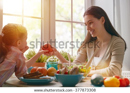 Happy family having dinner together sitting at the rustic wooden table. Mother and her daughter enjoying family dinner together.