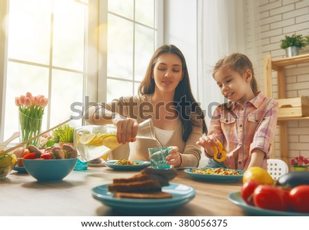 Happy family having dinner together sitting at the rustic wooden table. Mother and her daughter enjoying family dinner together.