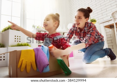 Happy family cleans the room. Mother and daughter do the cleaning in the house. A young woman and a little child girl having fun and riding in cardboard boxes at home.