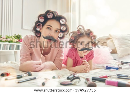 Funny family Mother and her child daughter girl with a paper accessories. Mother and daughter preparing for a party and having fun. Beautiful young woman and funny girl with a paper mustache on stick.
